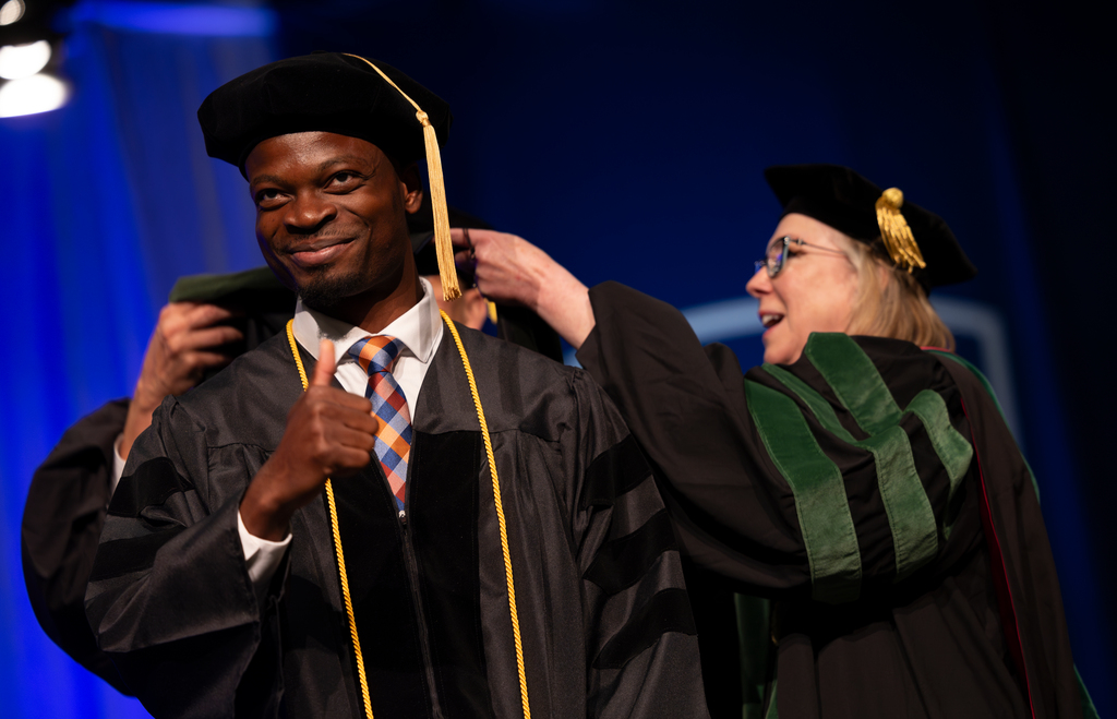 A medical student smiles while being a hooded by a faculty member
