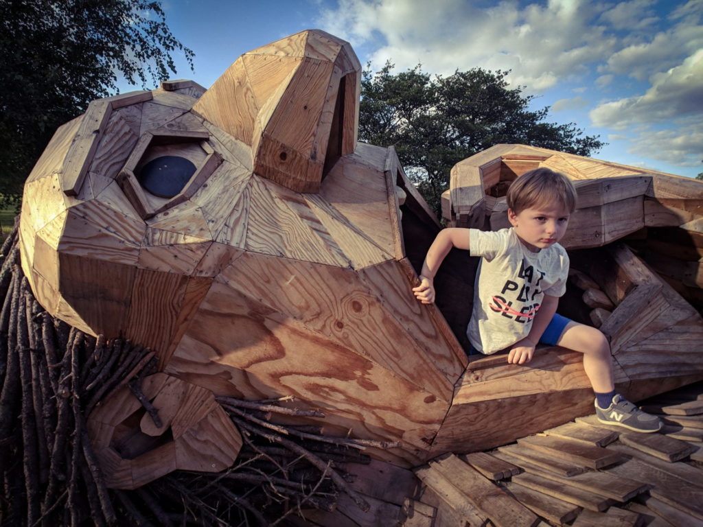 A young boy is seen climbing in a wooden structure shaped like a lying-down person. The boy is climbing out of the structure's mouth. The photo is by Suzanne Boltz and appears in the 2020 edition of Wild Onions, Penn State College of Medicine's art and literary journal.