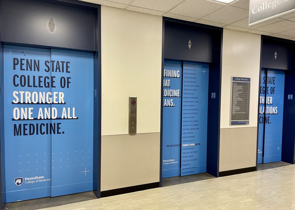 Elevators doors inside the College of Medicine are wrapped with branding including 'Penn State College of Stronger One And All Medicine'